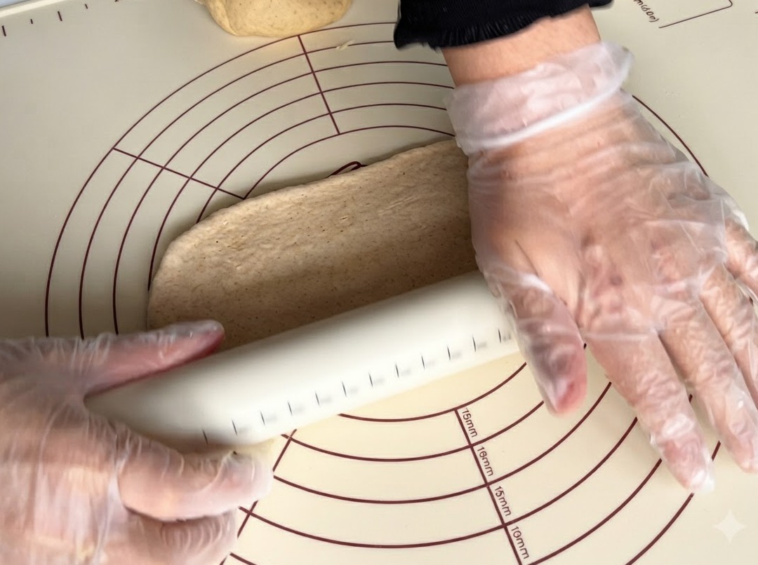 Un rouleau à pâtisserie aplatissant un morceau de pâte complète sur un tapis en silicone.