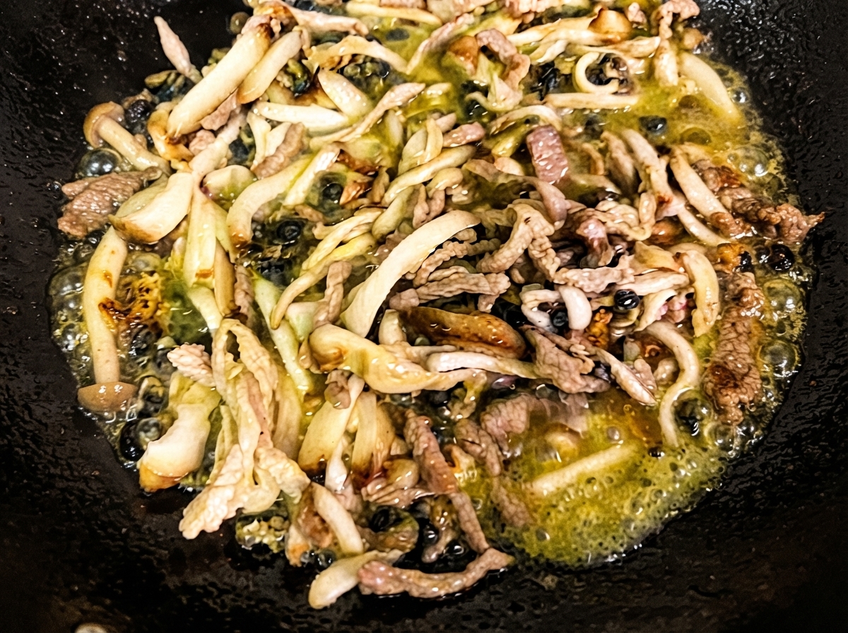 Champignons shiitake et enoki émincés et bulots de mer en train de sauter dans de lhuile chaude à lintérieur dun wok noir.