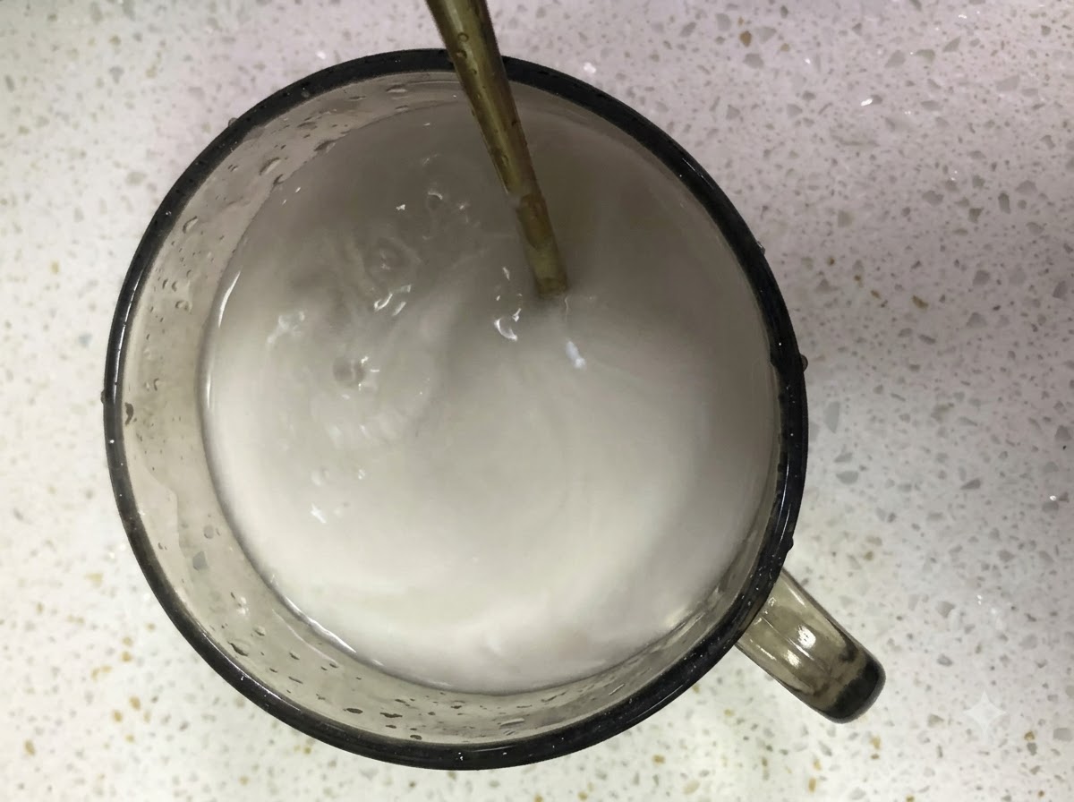 Mélange de fécule de patate douce et deau remué dans un verre avec une cuillère.