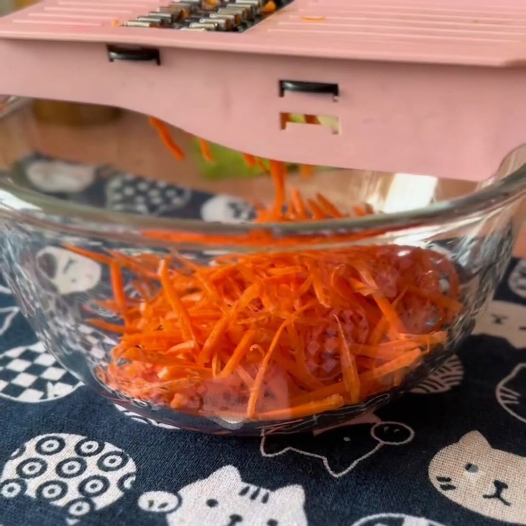 Carottes et concombres frais râpés à laide dune mandoline rose dans un bol en verre.