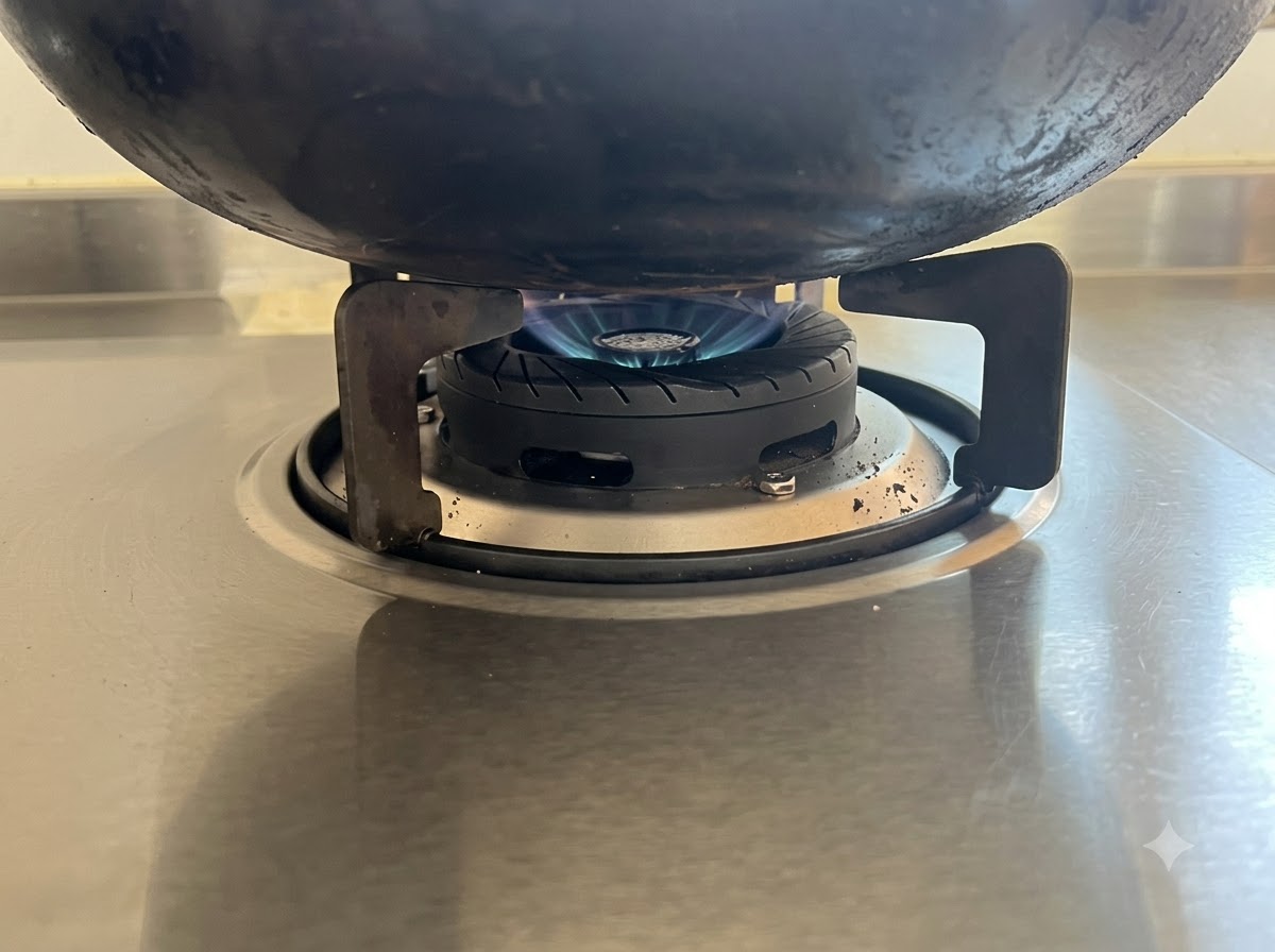Une flamme bleue basse chauffant le fond dun wok noir sur une cuisinière en acier inoxydable.