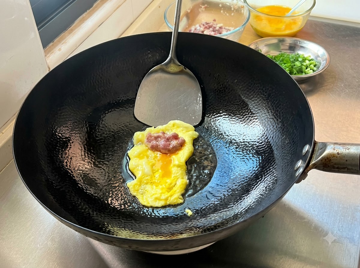 Une portion de farce de viande assaisonnée reposant sur une crêpe aux œufs fine fraîchement cuite dans un wok chaud, prête à être pliée.