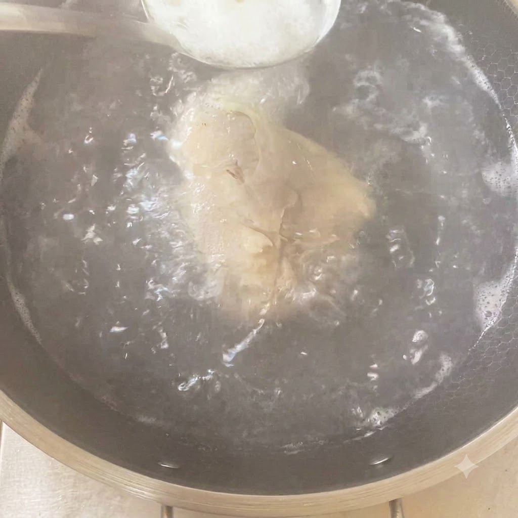 Une cuillère dassaisonnement ajoutée dans une casserole bouillante contenant le poulet et les aromates.