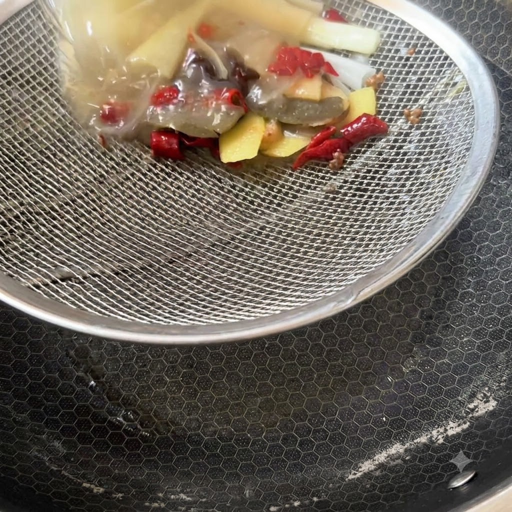 Une passoire attrapant les restes dépices, les tranches de gingembre et les résidus de piment au-dessus dune casserole vide.