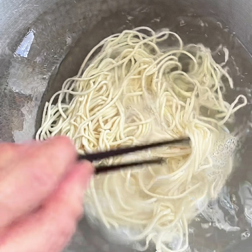 Des nouilles cuisant dans une casserole et remuées avec des baguettes.