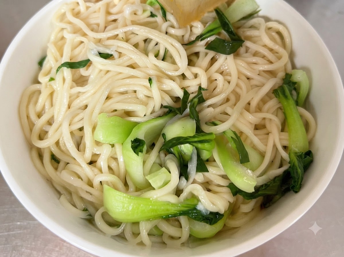 Des nouilles cuites et du bok choy frais disposés dans un bol de service blanc.