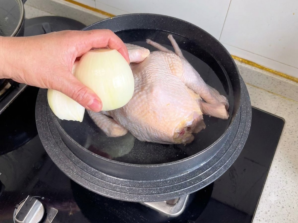 Une moitié doignon et dautres aromates jetés dans une casserole contenant un poulet entier et de leau.