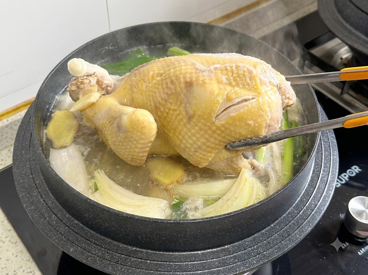 Des pinces de cuisine saisissant et retournant un poulet entier dans une casserole de bouillon bouillant.