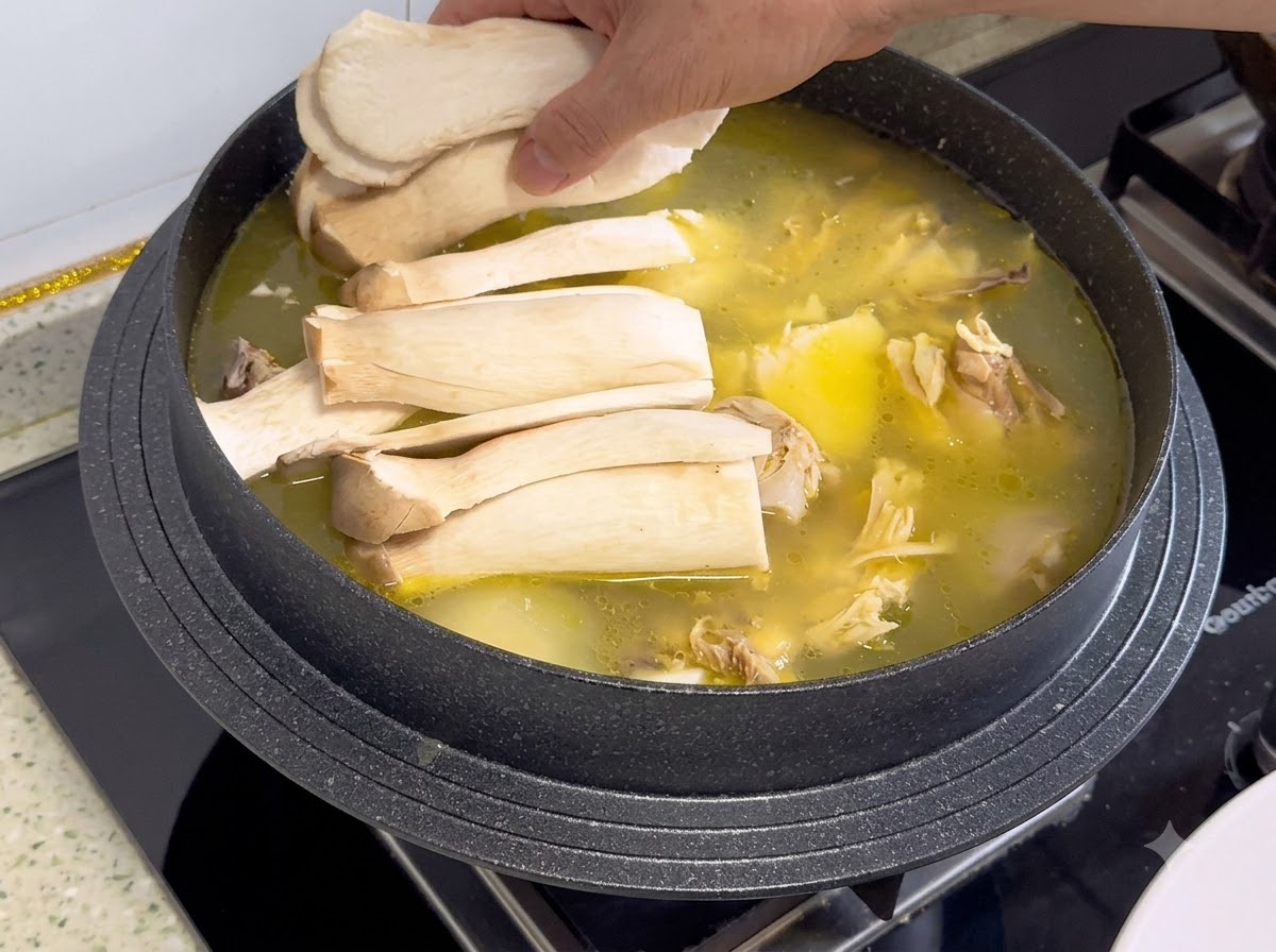 Des tranches de champignons eryngii disposées sur le bouillon de poulet et les ingrédients dans une casserole.