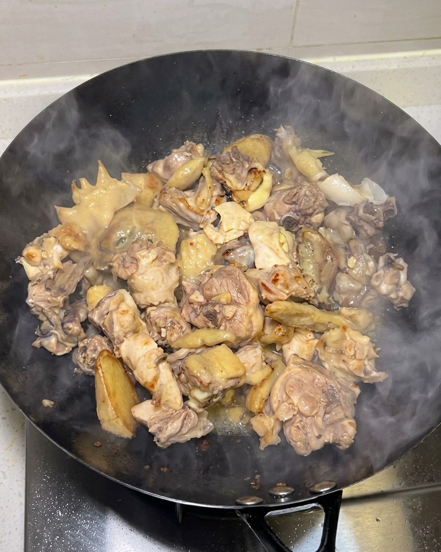 Morceaux de poulet saisis dorés en cours de cuisson dans un wok avec de la vapeur qui sélève.