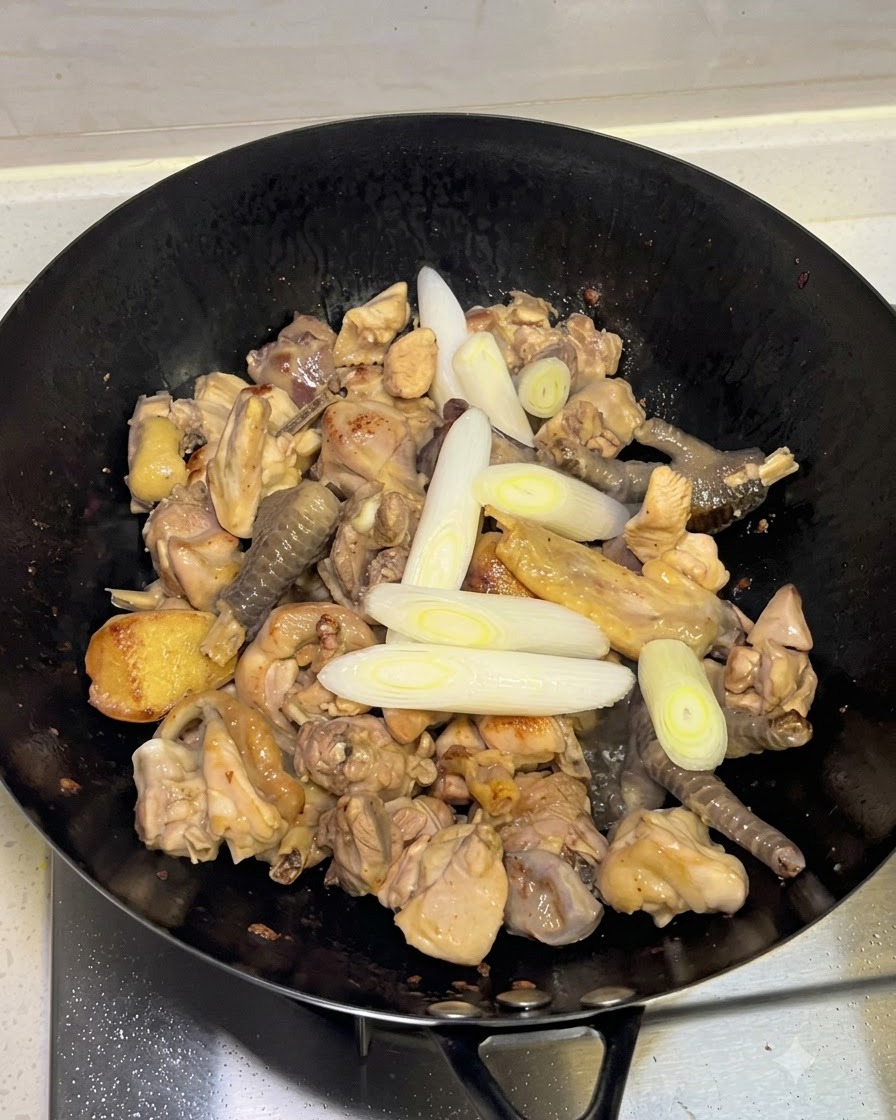 Ajout de ciboulettes, dail et dépices entières dans le wok avec le poulet.