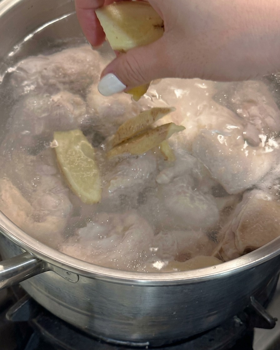 Une main jetant des tranches de gingembre frais dans une casserole deau bouillante avec du poulet.