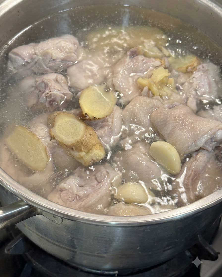Gousses dail et tranches de gingembre flottant dans la casserole avec des morceaux de poulet dans leau frémissante.