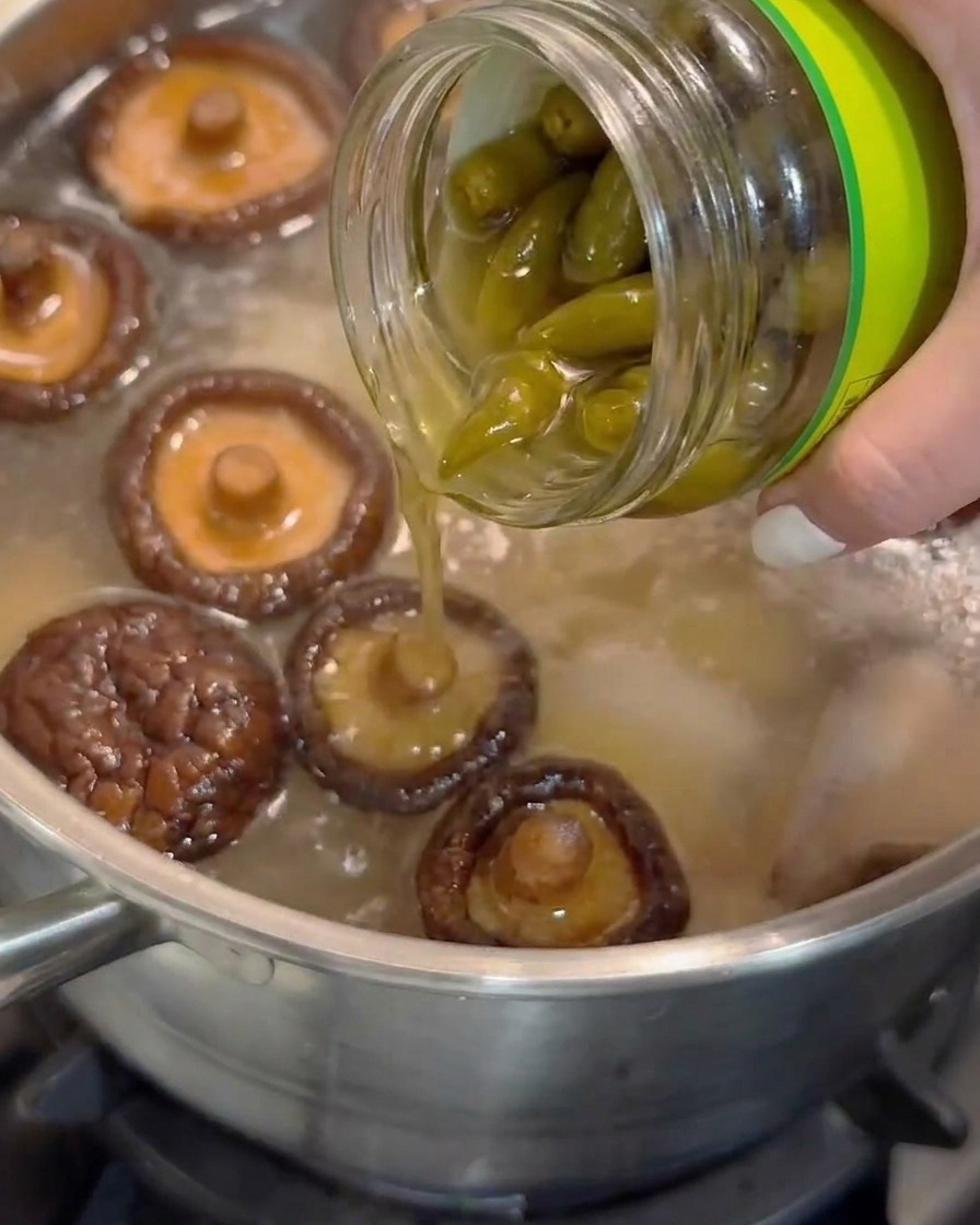 Jus de piment vert pelé mariné versé dun bocal en verre dans une casserole de soupe frémissante avec des champignons shiitakes.