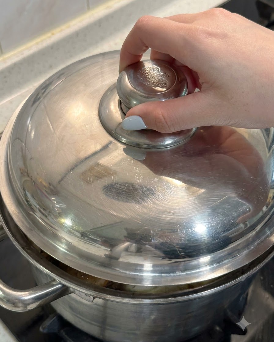 Une main plaçant le couvercle en métal sur une casserole remplie de poulet et dingrédients de soupe.