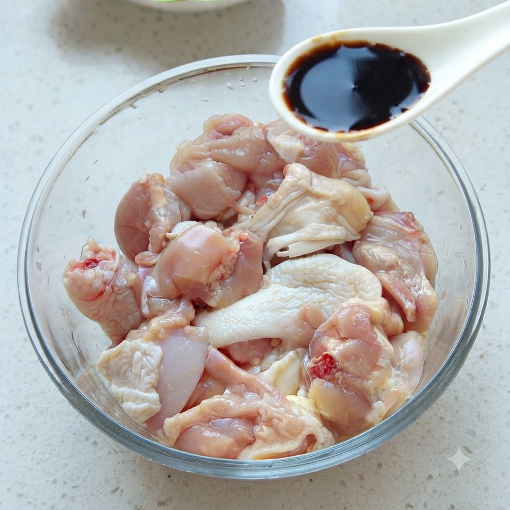 Une cuillère de sauce soja foncée ajoutée dans un bol en verre rempli de morceaux de poulet cru.