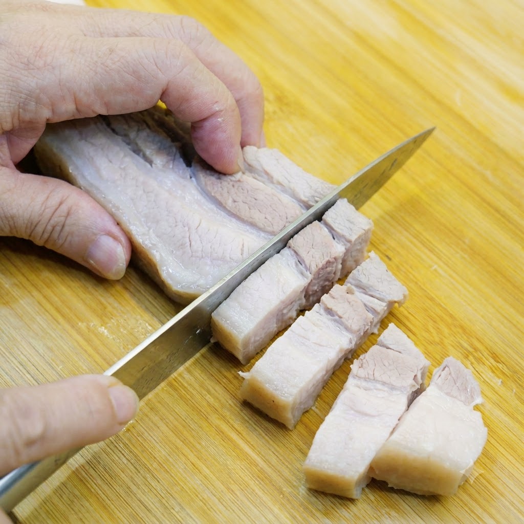 Poitrine de porc blanchie coupée en morceaux de taille idéale sur une planche en bois.