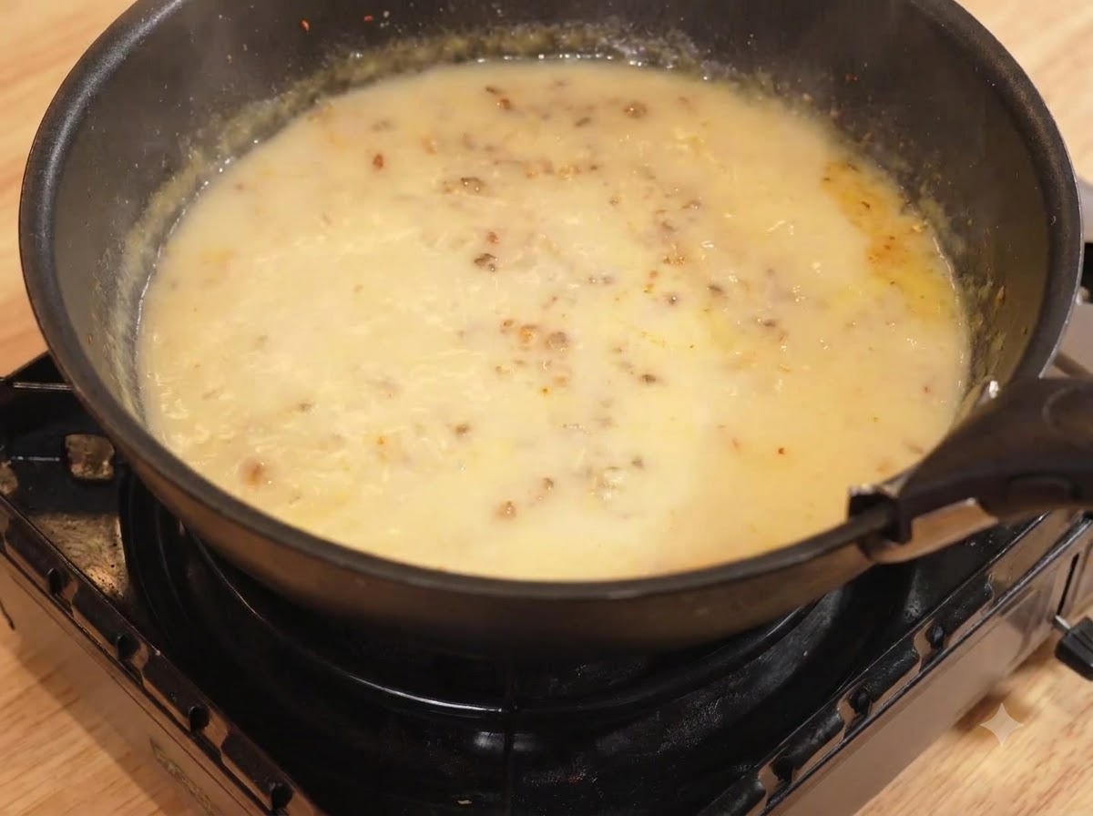 Eau et lait versés dans la poêle avec le mélange de curry, mijotant à feu doux.