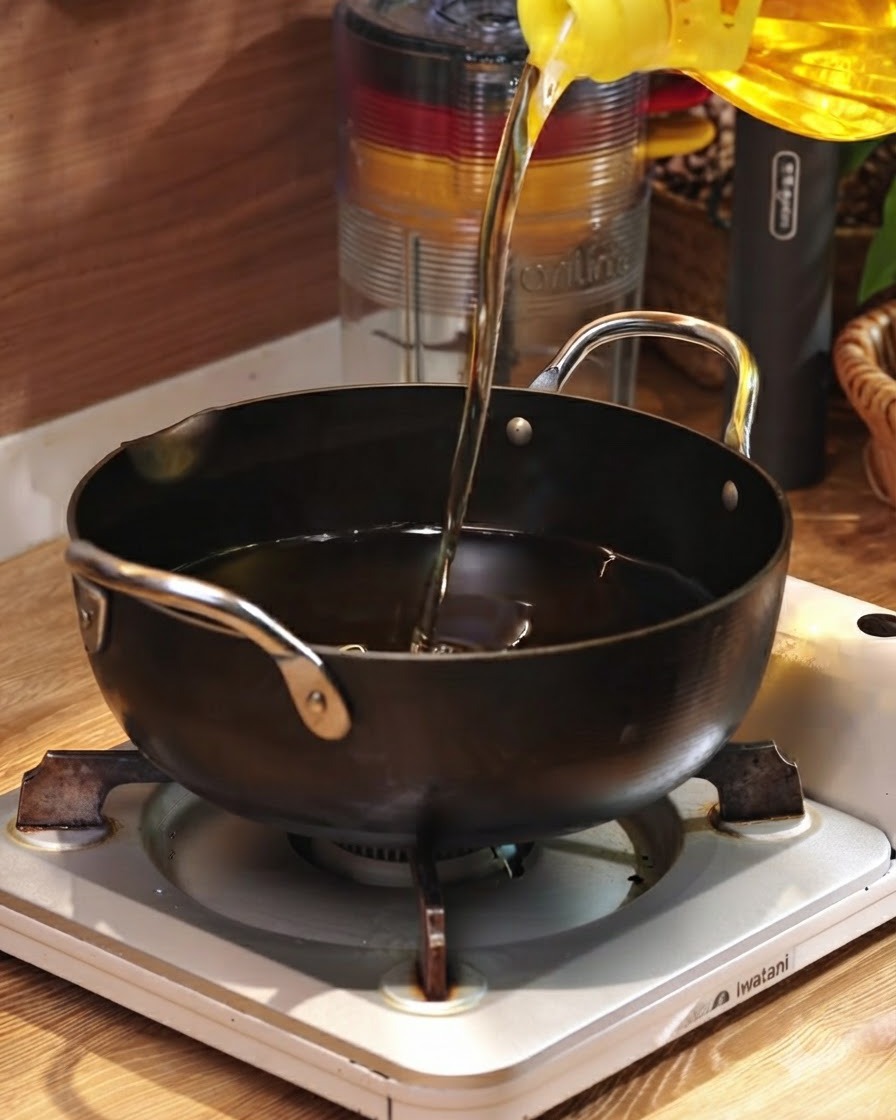 Huile de cuisson versée dun récipient jaune dans une poêle noire posée sur un brûleur portable.