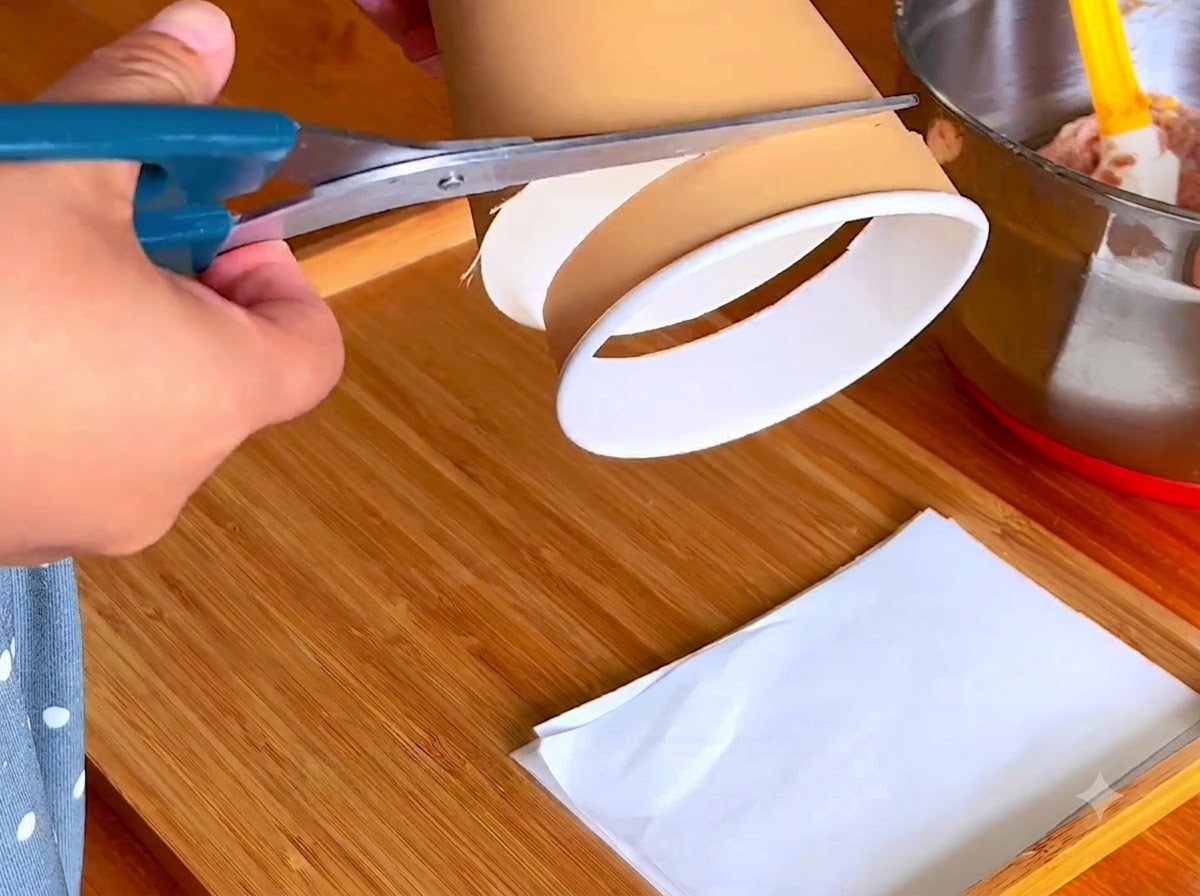 Une paire de ciseaux bleus coupant le bord inférieur dun gobelet en papier sur une planche en bois.