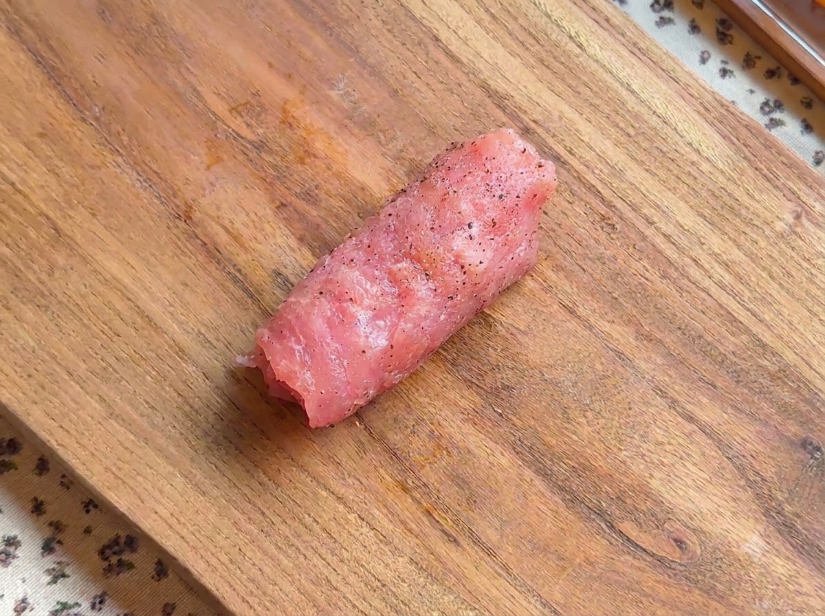 Un rouleau descalope de porc assaisonné reposant sur une planche en bois.