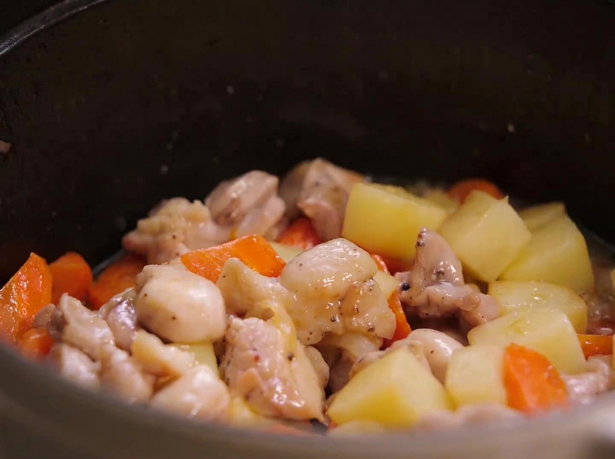 Morceaux de poulet poêlés, morceaux de pommes de terre et de carottes mélangés à lintérieur dune cocotte.