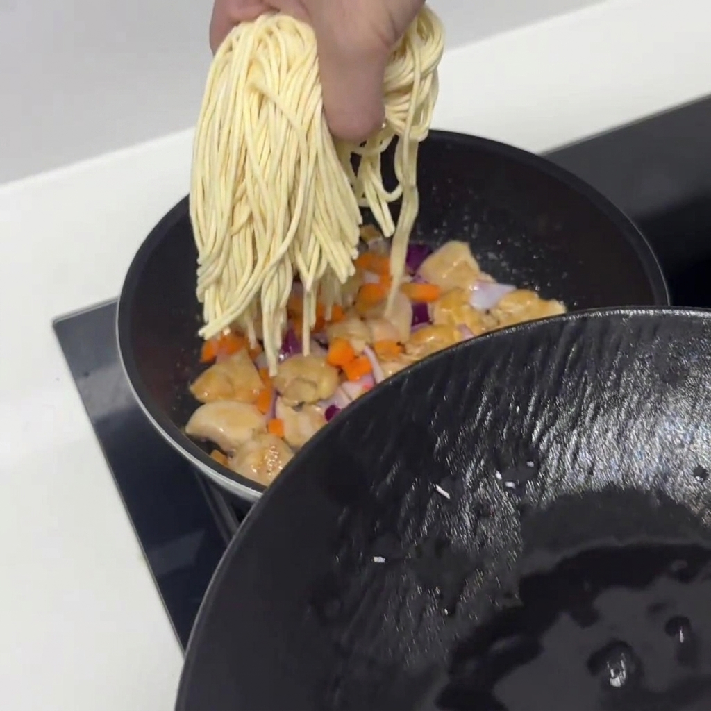 Nouilles de pâtes pré-trempées ajoutées dans la poêle avec le poulet et les légumes.