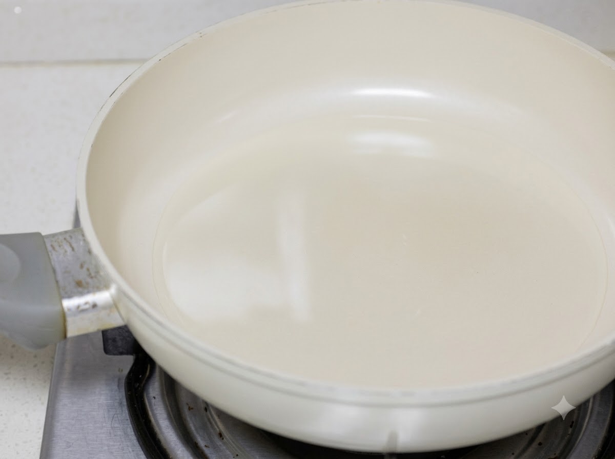 Morceaux de poulet en train dêtre saisis dans de lhuile de cuisson à lintérieur dune poêle blanche.