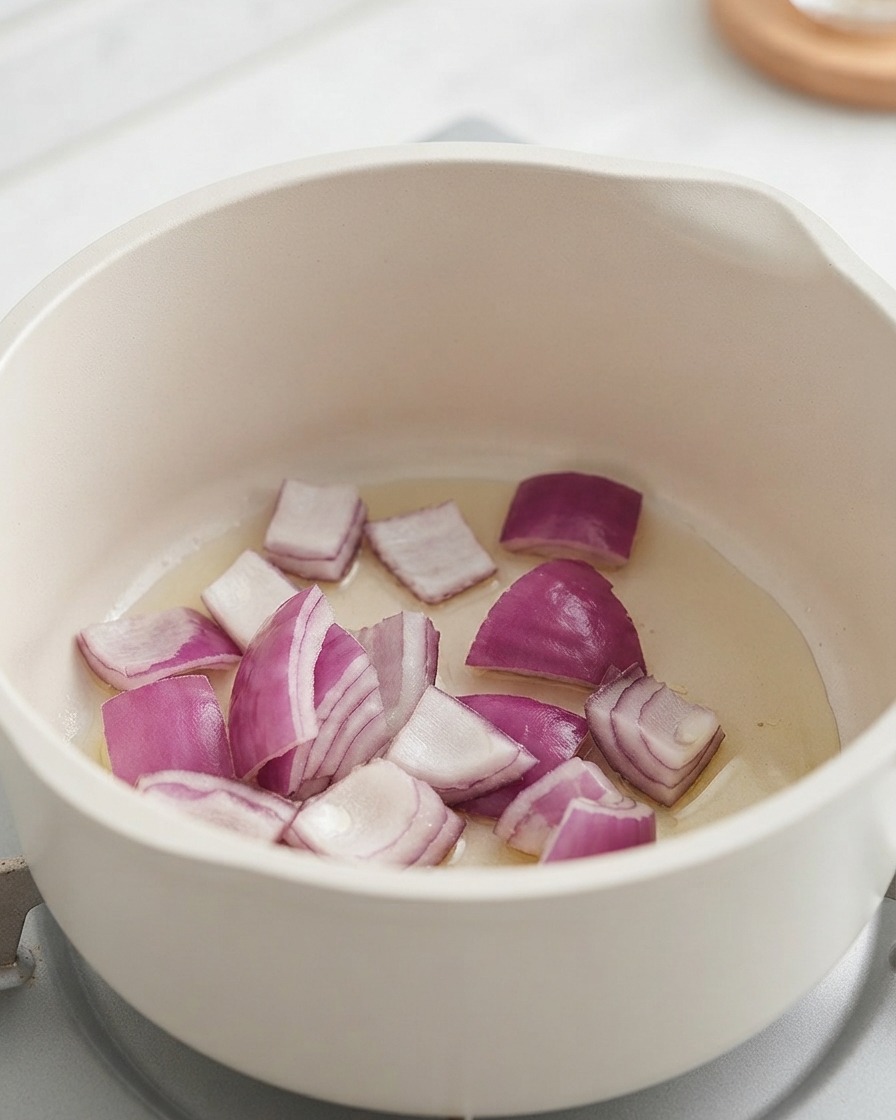 Oignons rouges hachés et pommes de terre cuisant à lintérieur dune casserole blanche.