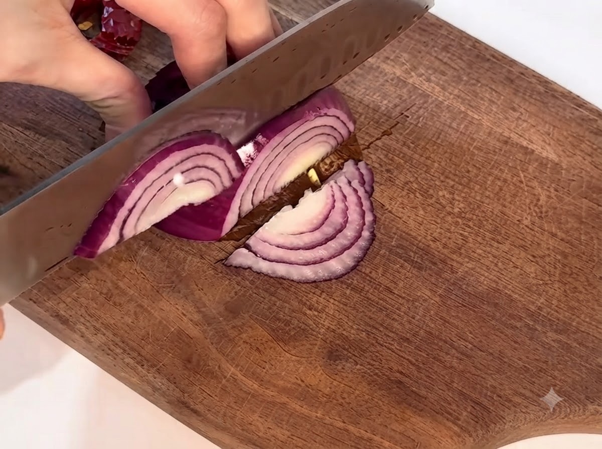 Un oignon rouge coupé soigneusement sur une planche à découper en bois avec un couteau.