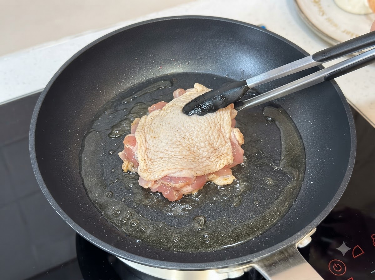 Une cuisse de poulet assaisonnée qui frit côté peau dans une poêle chaude huilée à laide de pinces.