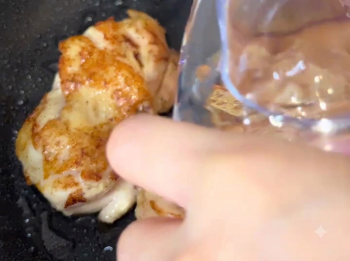 De leau versée dun récipient directement dans une poêle contenant des morceaux de poulet en train de frire.