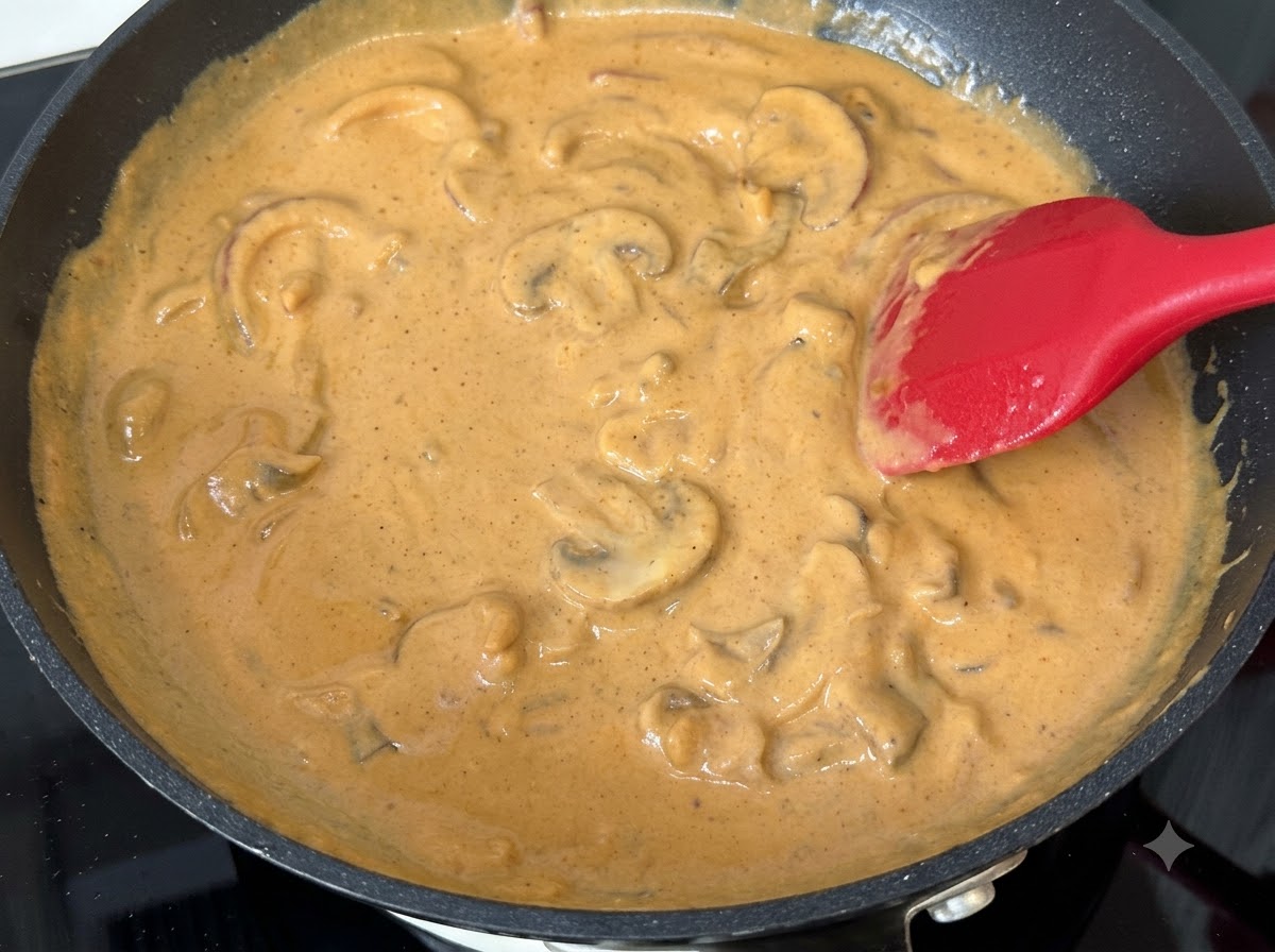 Tranches de champignons mélangées dans une sauce au curry et à la crème frémissante dans une poêle.