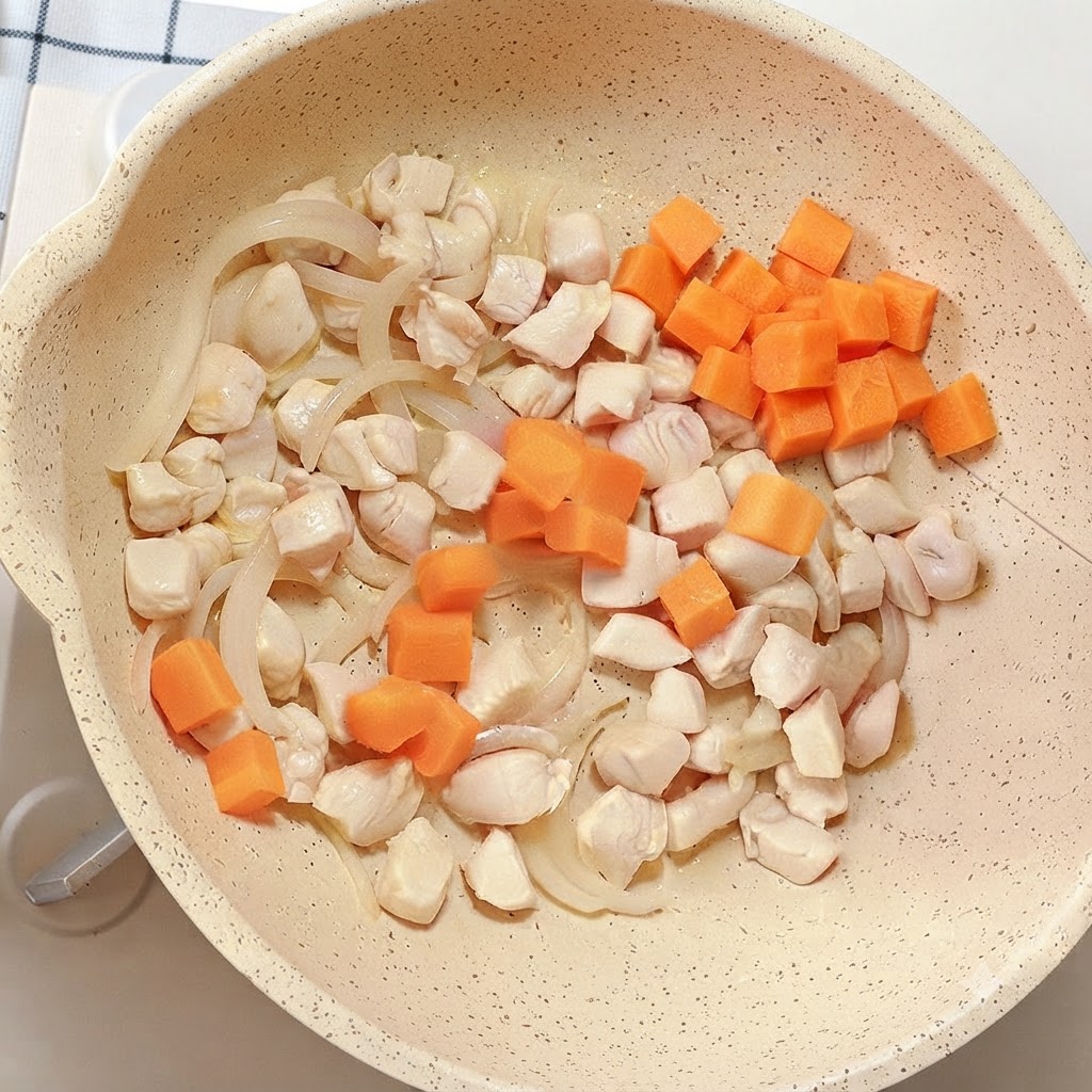 Dés de carottes orange vif ajoutés dans la poêle contenant le poulet et les oignons.