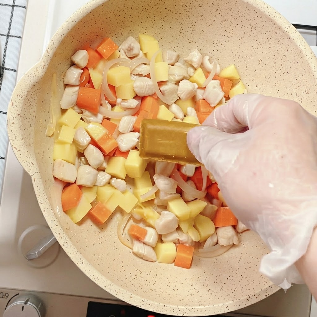 Une main plaçant un bloc de curry dans la poêle remplie de légumes mélangés et de poulet.