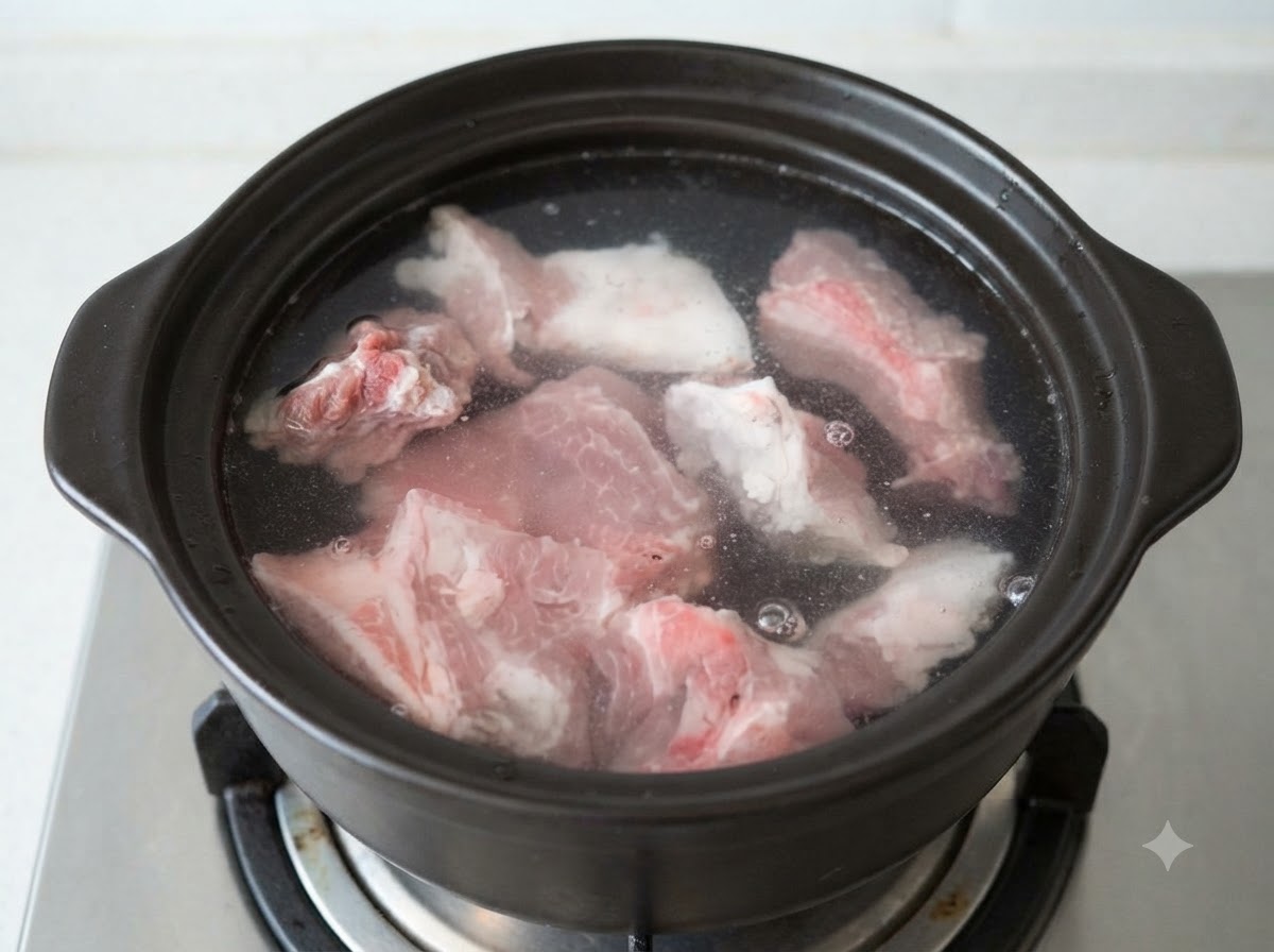 Morceaux dos de porc crus submergés dans de leau froide à lintérieur dun pot en terre cuite sombre.