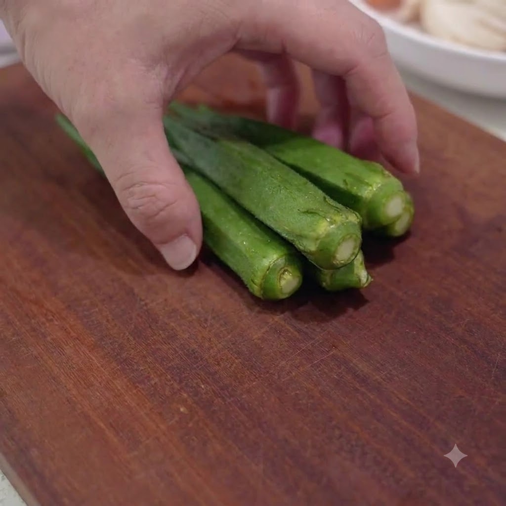 Gousses de gombos verts frais en train dêtre coupées en petits morceaux sur une planche à découper en bois.