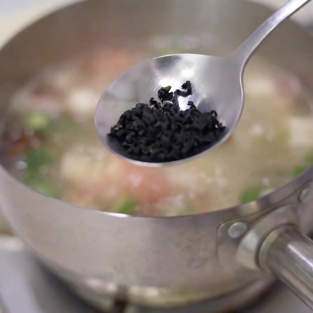 Une cuillerée de flocons dalgues séchées jetée dans une casserole de soupe frémissante en acier inoxydable.