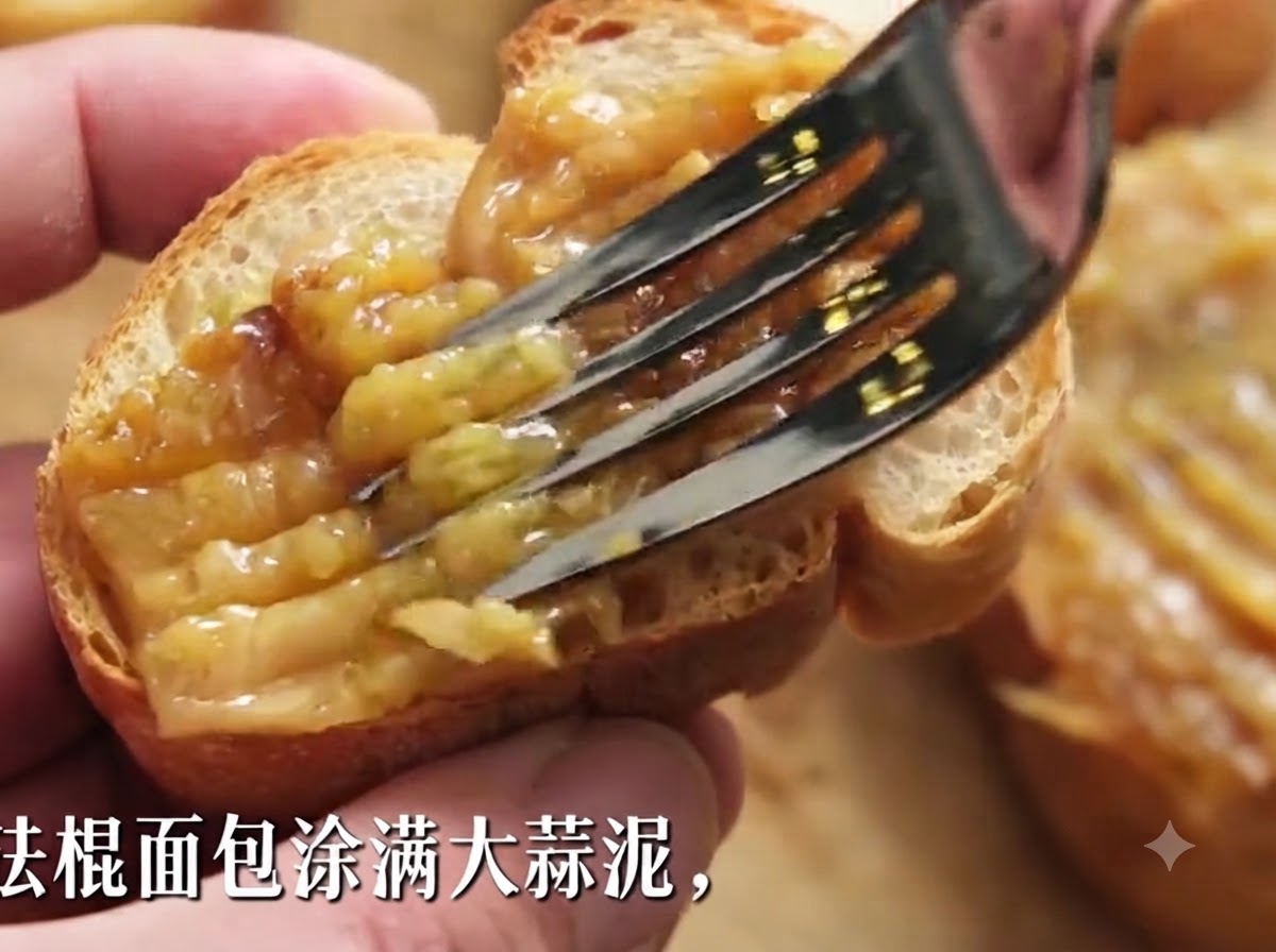Une fourchette étalant une épaisse pâte dail rôti sur une tranche de baguette croustillante.