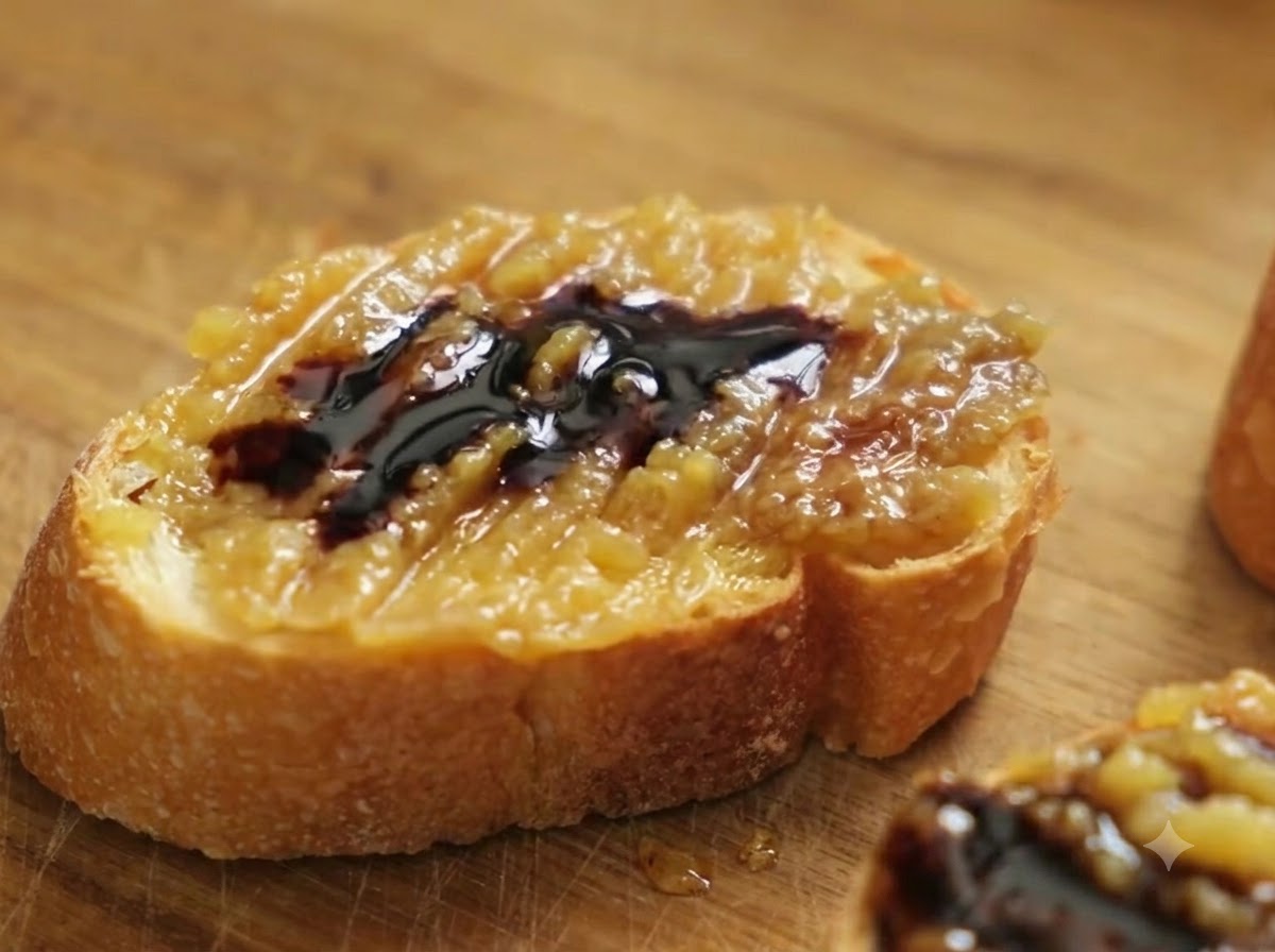 Gros plan dune tranche de baguette garnie de pâte de confit dail et de vinaigre balsamique, avec du gros sel de mer parsemé par-dessus.