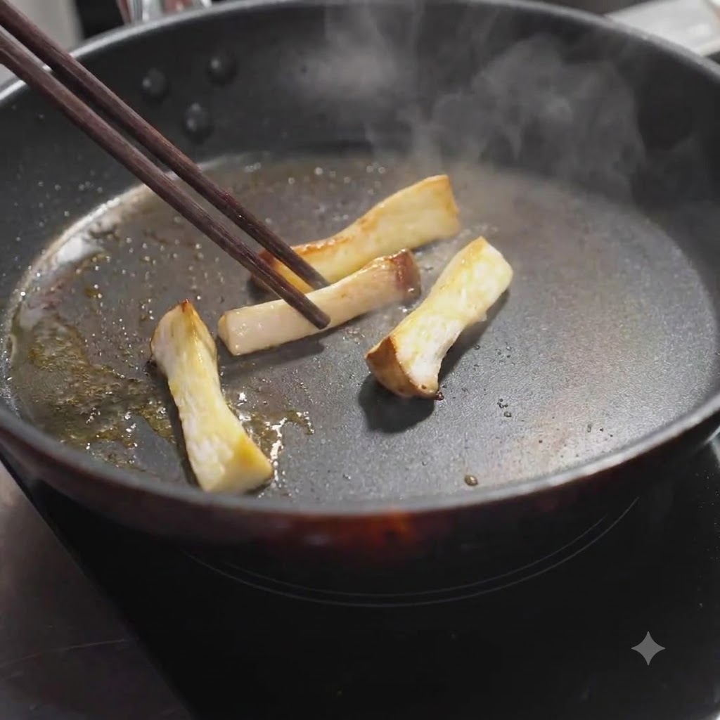 Des tranches de pleurotes royaux retournées dans la poêle avec des baguettes jusquà dorure.