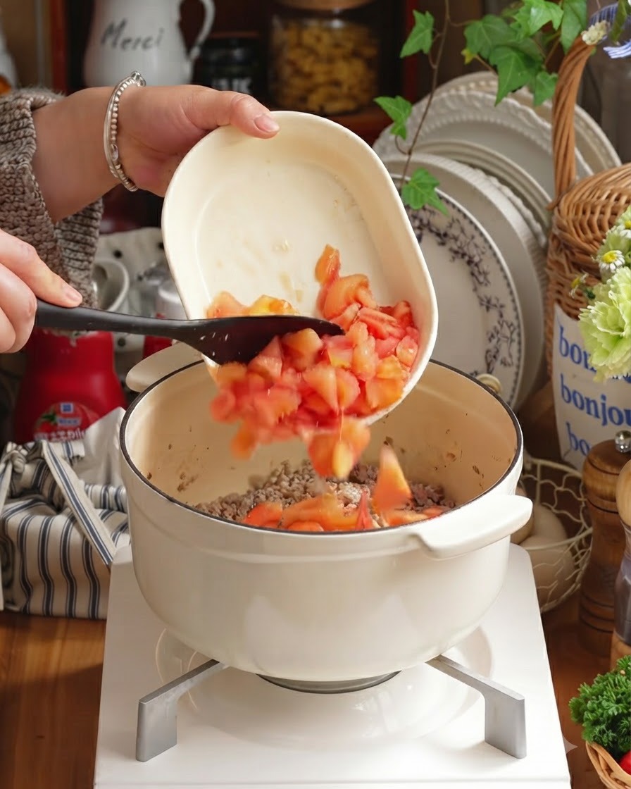 Tomates pelées en dés et légumes hachés ajoutés dans la casserole sur la viande.