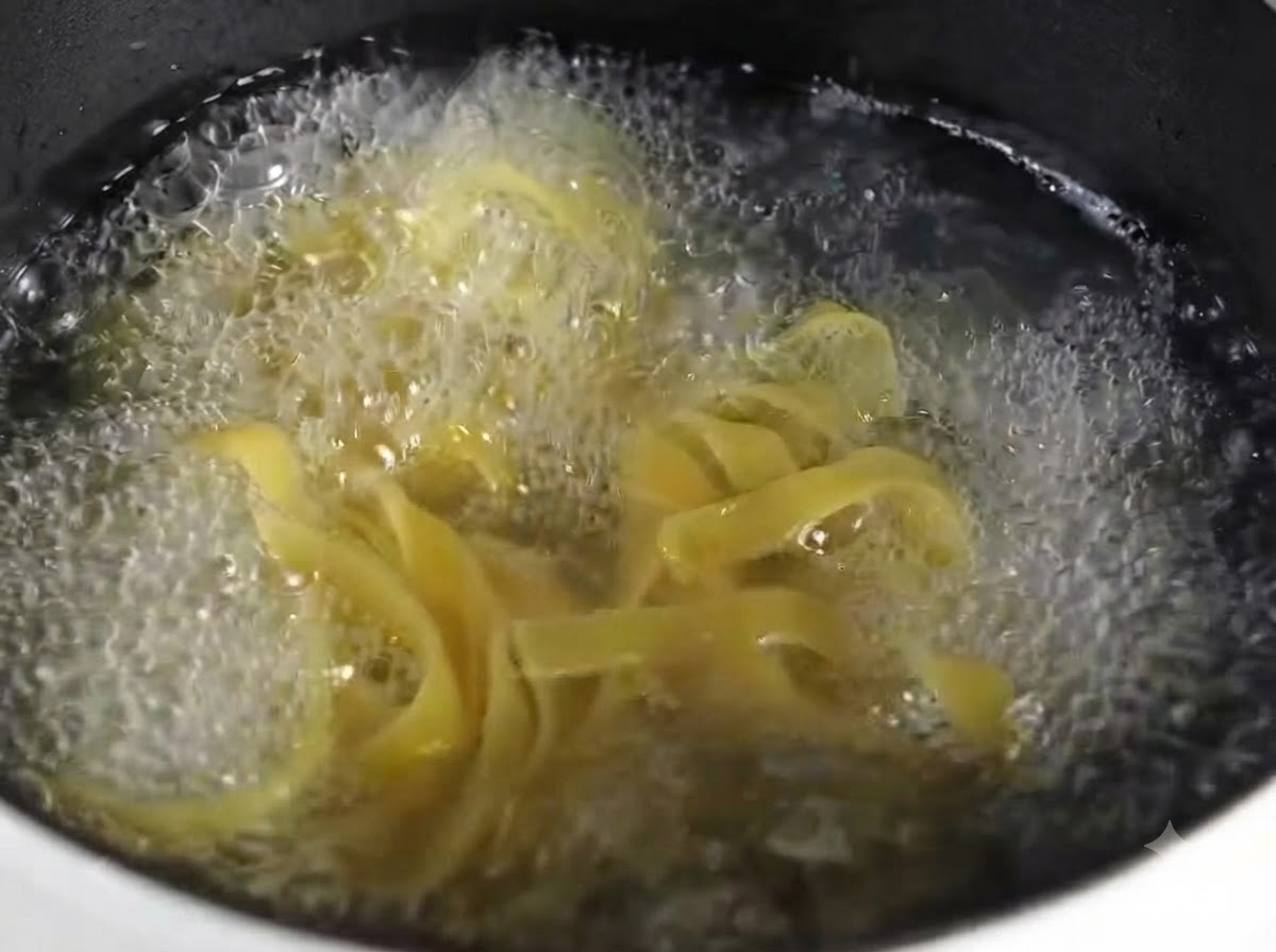 Vue rapprochée de fettuccine cuites disposées proprement sur une assiette grise ronde.