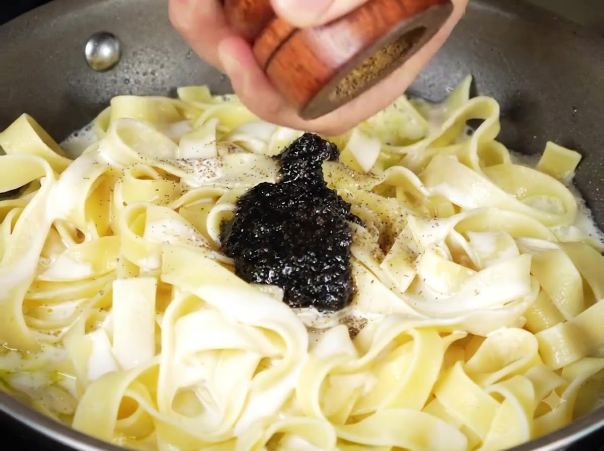 Sauce à la truffe noire et poivre fraîchement moulu sur les pâtes crémeuses dans la poêle.