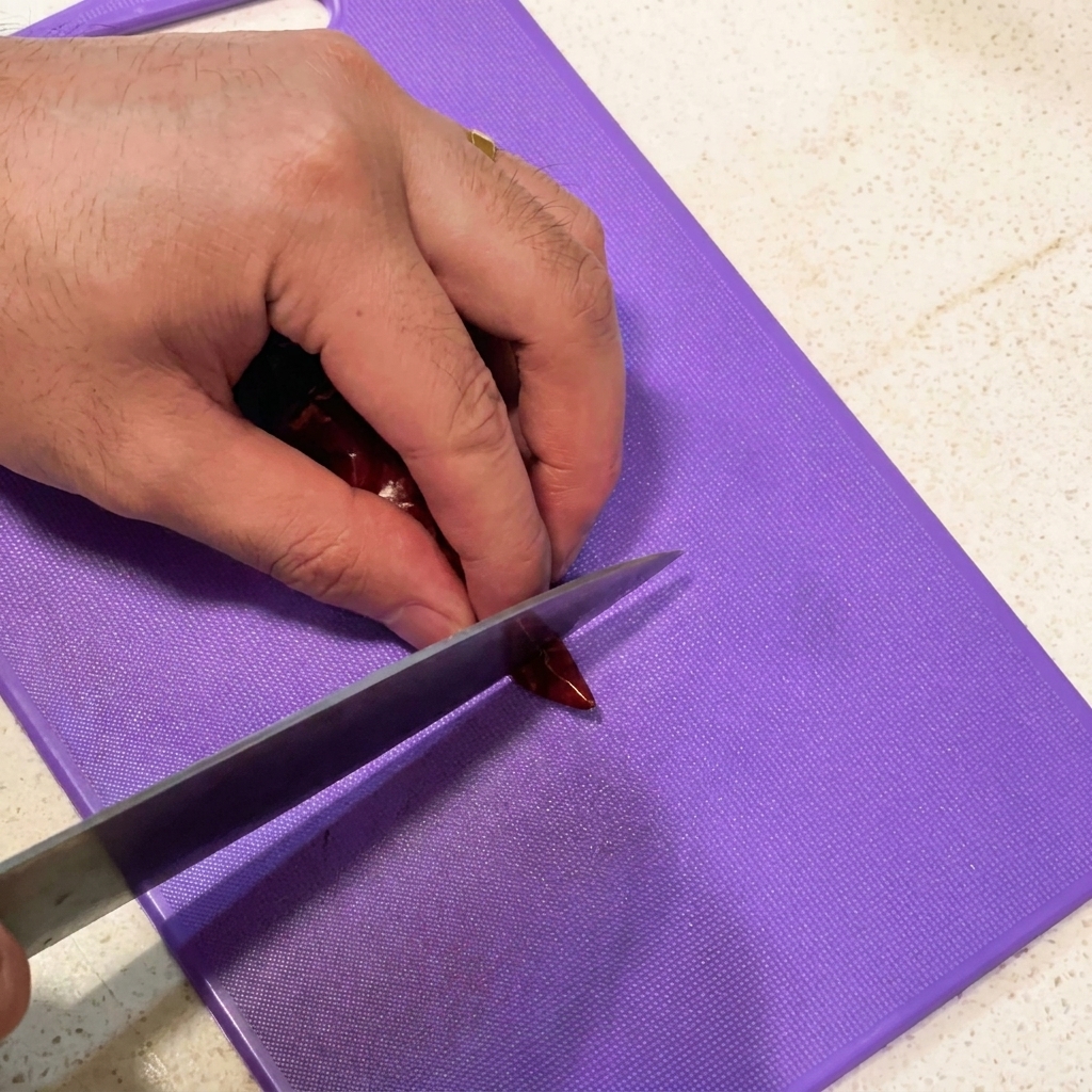 Trancher des gousses dail et couper des piments séchés en morceaux sur une planchette violette.