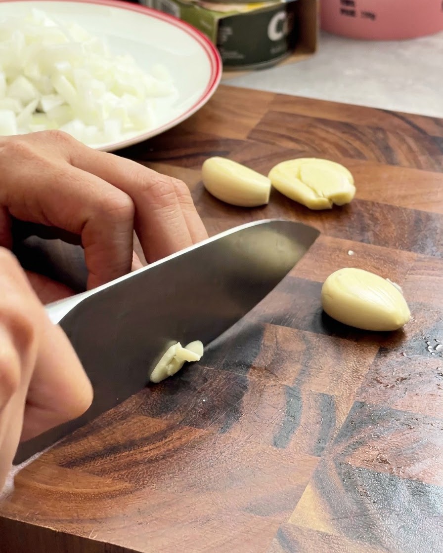 Des gousses dail hachées avec un couteau de chef sur une surface en bois.
