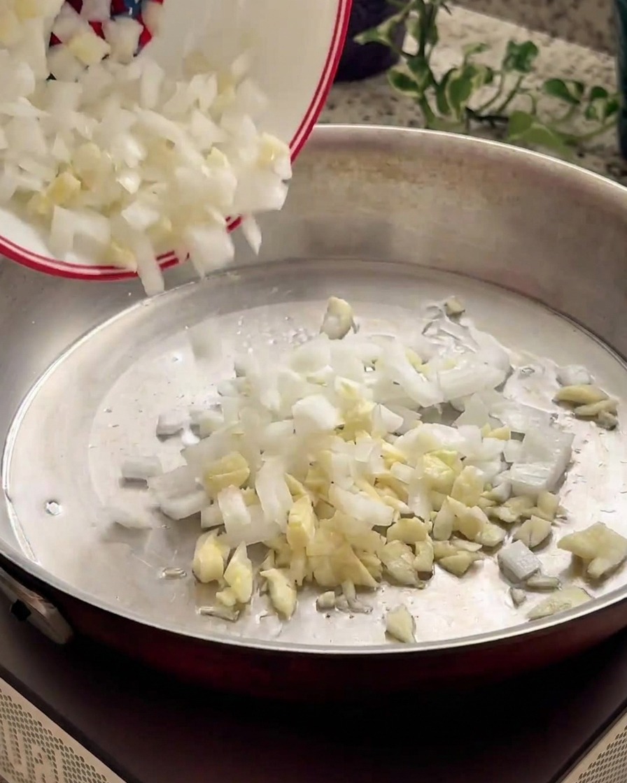 Des oignons et de lail hachés glissant dun petit bol blanc vers une poêle chaude en métal.