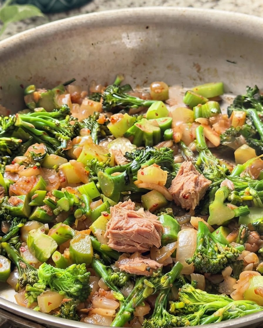 Des morceaux de thon en boîte mélangés dans la poêle avec le brocoli vert et les oignons.