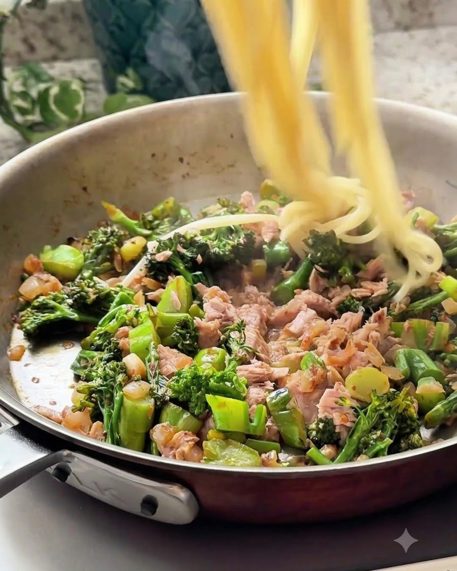Des brins de spaghetti cuits versés dans la poêle avec le mélange de thon et de légumes.