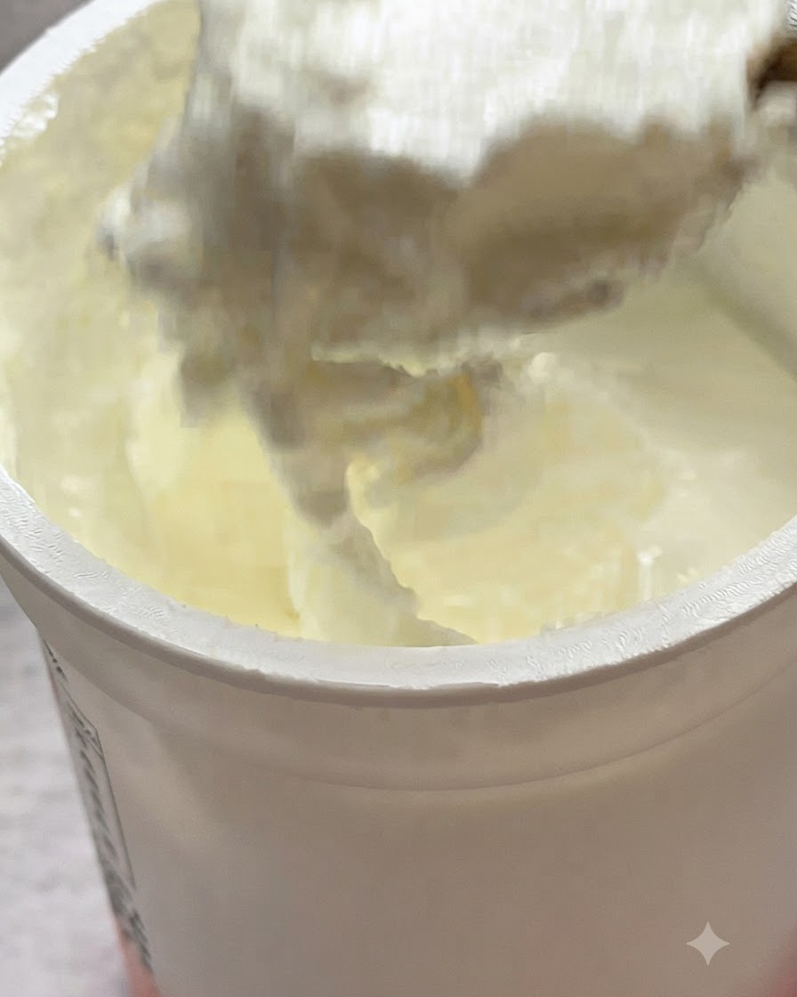 Une cuillère de yaourt nature ajoutée sur les pâtes dans une poêle.